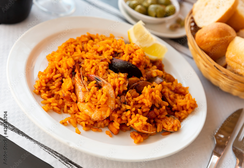 Traditional Valencian paella de mariscos with shrimps and mussels served with lemon on white plate