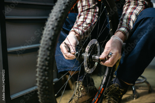 Technical expertise taking care bicycle shop. Handsome young mechanic fixing cycle wheel in workshop. Handsome repairman in workwear serving mountain bicycle. Male engineer adjusting velocipede