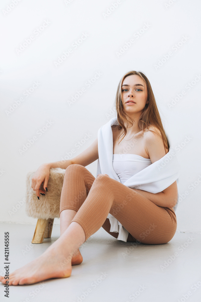 Young woman in white hoodie on shoulders beautiful fit girl in sport wear sitting on floor in the white studio Young woman in white hoodie on shoulders beautiful fit girl in sport wear sitting on floor in the white studio