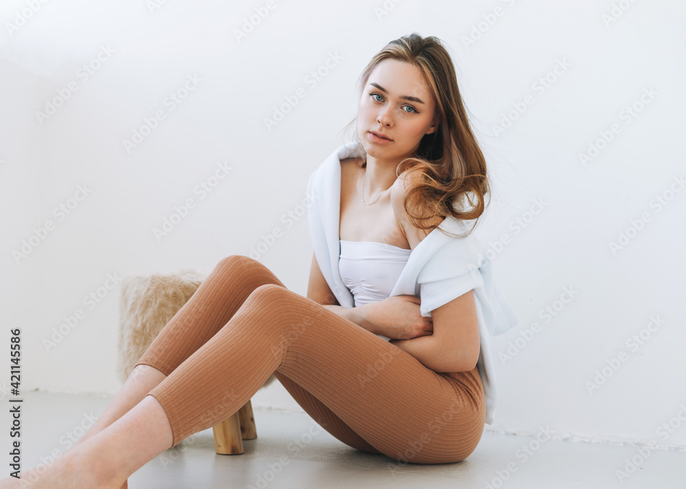 Young woman in white hoodie on shoulders beautiful fit girl in sport wear sitting on floor in the white studio