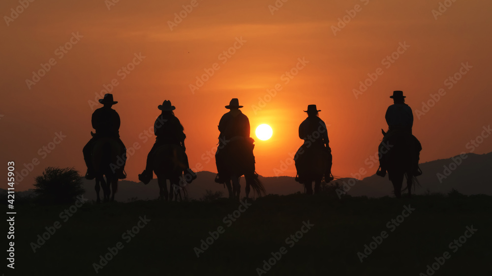 Vintage and silhouettes of a group of cowboys sitting on horseback at sunset.