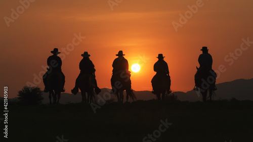 Fotografie, Obraz Vintage and silhouettes of a group of cowboys sitting on horseback at sunset