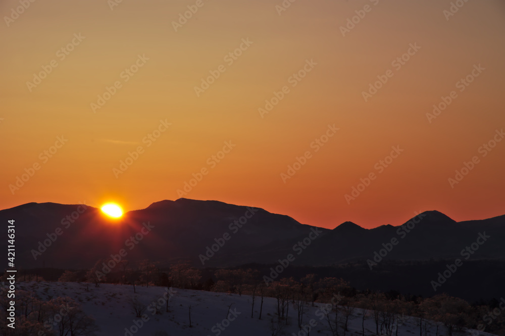 オレンジ色の夜明けの空と稜線から昇る朝陽。