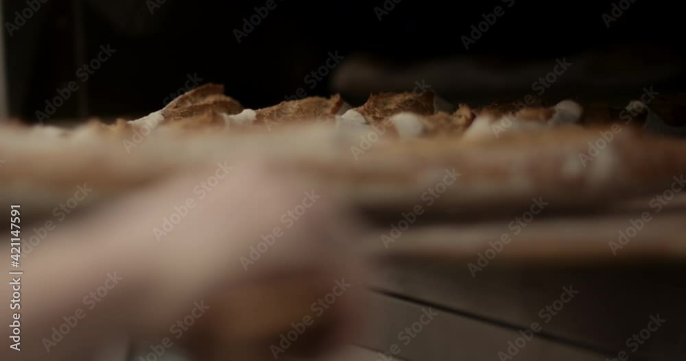 Close up of male baker taking freshly baked baguettes out of oven in bakery Close up of male baker taking freshly baked baguettes out of oven in bakery