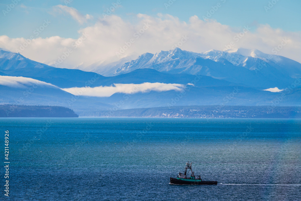 A fishing boat in Puget sound sailing in front of the Olympic Mountains
