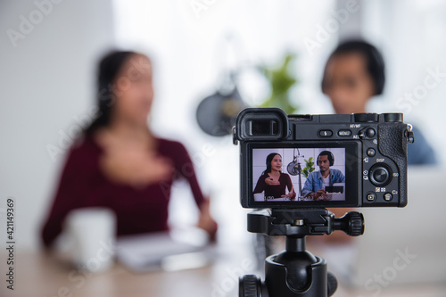 Close up camera of two Asian radio hosts recording podcast in broadcasting studio, Asian woman talking on microphone with man online at home