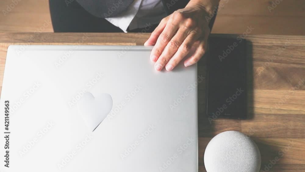 Eine Frau im Büro oder Homeoffice klappt den Laptop zu, auf dem ein Herz geklebt ist. Mit Liebe zum Beruf und mit viel Motivation. 