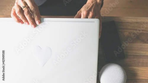 Eine Frau im Büro oder Homeoffice klappt den Laptop zu, auf dem ein Herz geklebt ist. Mit Liebe zum Beruf und mit viel Motivation. 