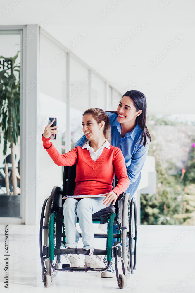 Young latin woman in wheelchair taking a selfie photo at workplace with another woman in Mexico Young latin woman in wheelchair taking a selfie photo at workplace with another woman in Mexico