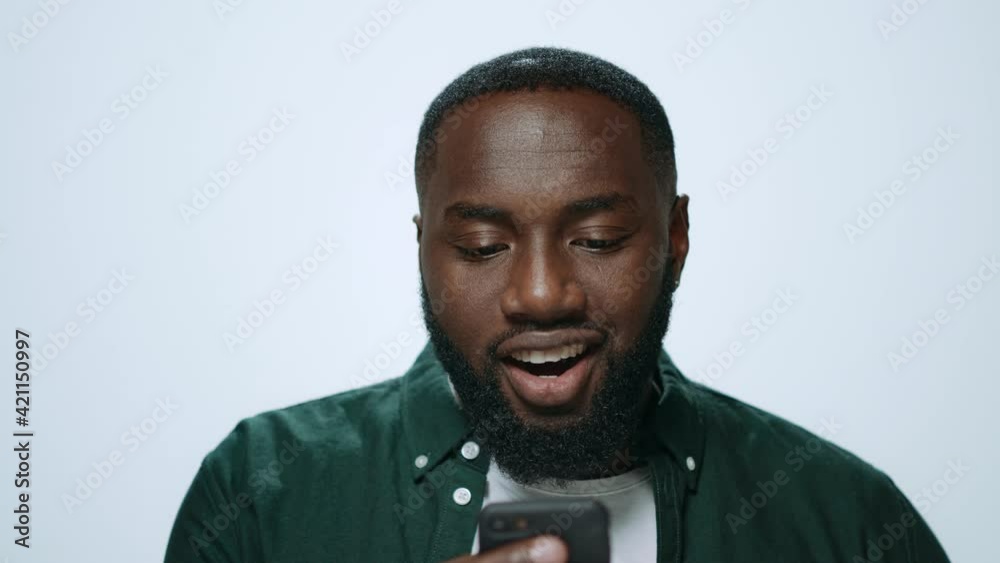 Portrait of emotional african man looking smartphone screen in grey background.