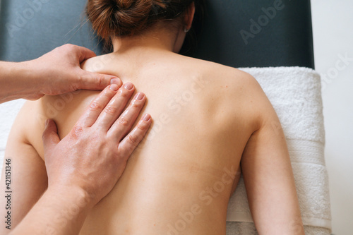 Top view of male masseur with strong hands professionally massaging scapulas and shoulders. Beautiful naked young woman with perfect skin getting back massage at spa salon.