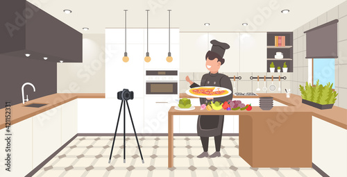 food blogger in uniform cooking pizza in kitchen male chef recording video blog with camera on tripod blogging concept man vlogger explaining how to cook a dish horizontal full length