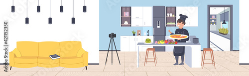 food blogger in uniform cooking pizza in kitchen male chef recording video blog with camera on tripod blogging concept man vlogger explaining how to cook a dish horizontal full length