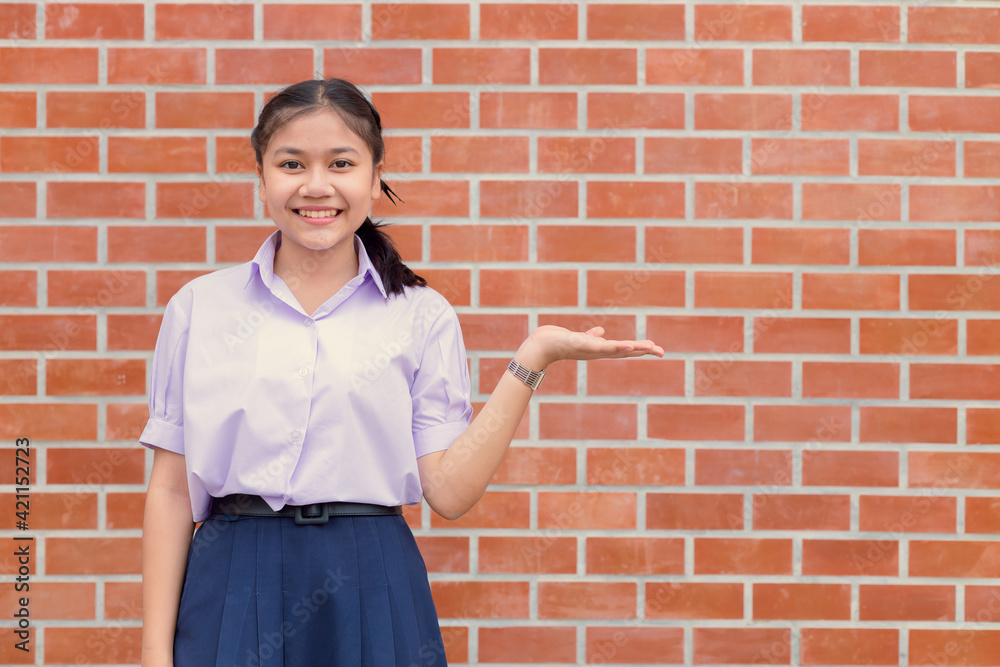 Asian girl teen student uniform happy smile with hand presentor showing display wall copy space. Asian girl teen student uniform happy smile with hand presentor showing display wall copy space.