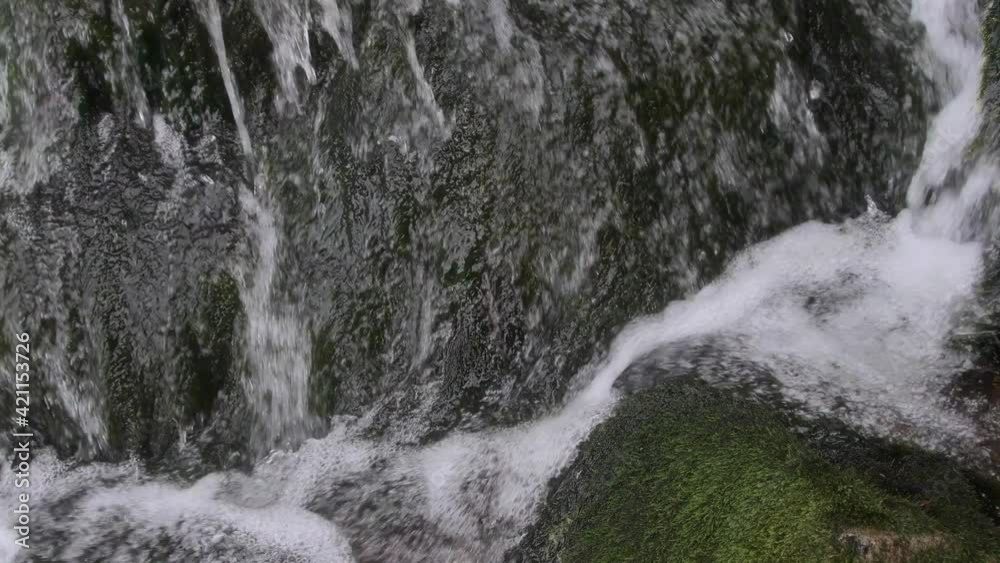Streams of water run down green moss of stone, forms bubbles and foam. Section of mountain river in close up. Structure of flow at boulders Streams of water run down green moss of stone, forms bubbles and foam. Section of mountain river in close up. Structure of flow at boulders