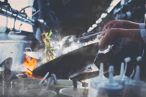 Chef stir fry busy cooking in kitchen. Chef stir fry the food in a frying pan, smoke and splatter the sauce in the kitchen. photo