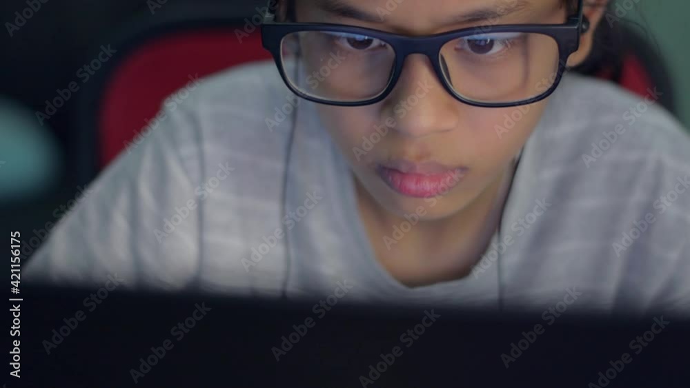 Close up adorable young girl face in eyeglasses wearing earphone watching laptop monitor during learning video tutorial for education at home. Internet technology with social online network. Close up adorable young girl face in eyeglasses wearing earphone watching laptop monitor during learning video tutorial for education at home. Internet technology with social online network.