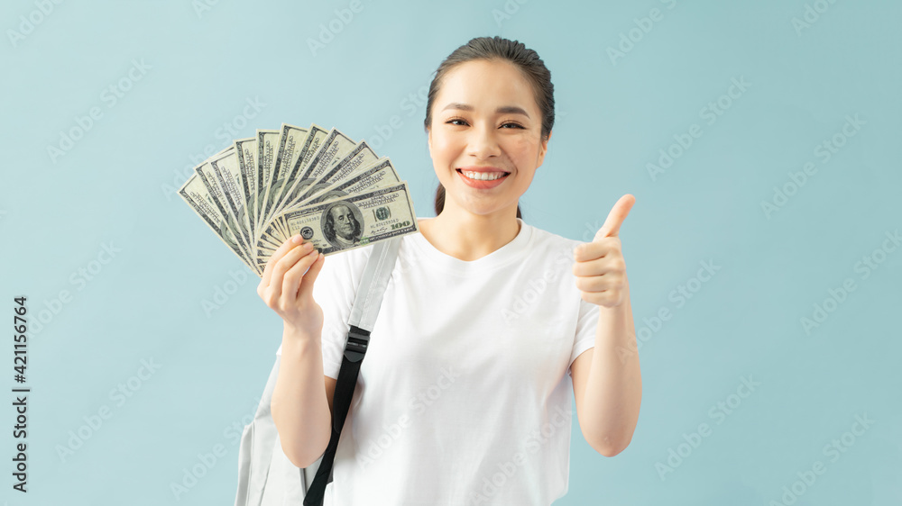 Funny girl student with backpack, holding fan of cash money in dollar banknotes showing thumb up Funny girl student with backpack, holding fan of cash money in dollar banknotes showing thumb up