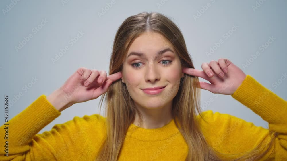 Portrait of smiling woman covers her ears with fingers at camera in studio. Portrait of smiling woman covers her ears with fingers at camera in studio.