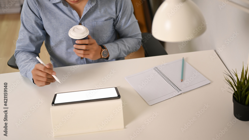 Cropped shot of businessman holding coffee cup and working on digital tablet. Cropped shot of businessman holding coffee cup and working on digital tablet.