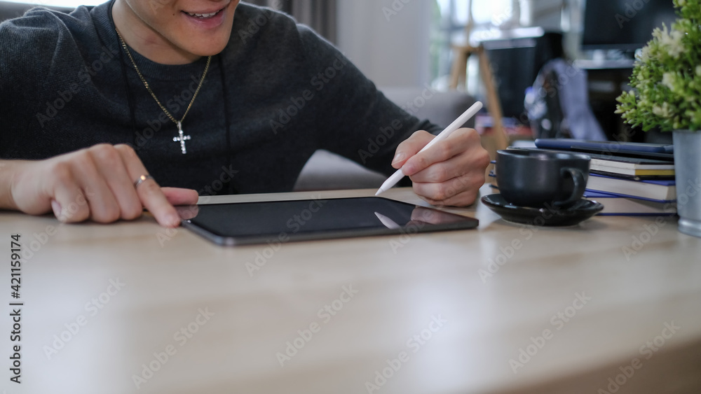 Obraz premium Cropped shot of happy young man freelancer holding stylus pen writing on screen of digital tablet.