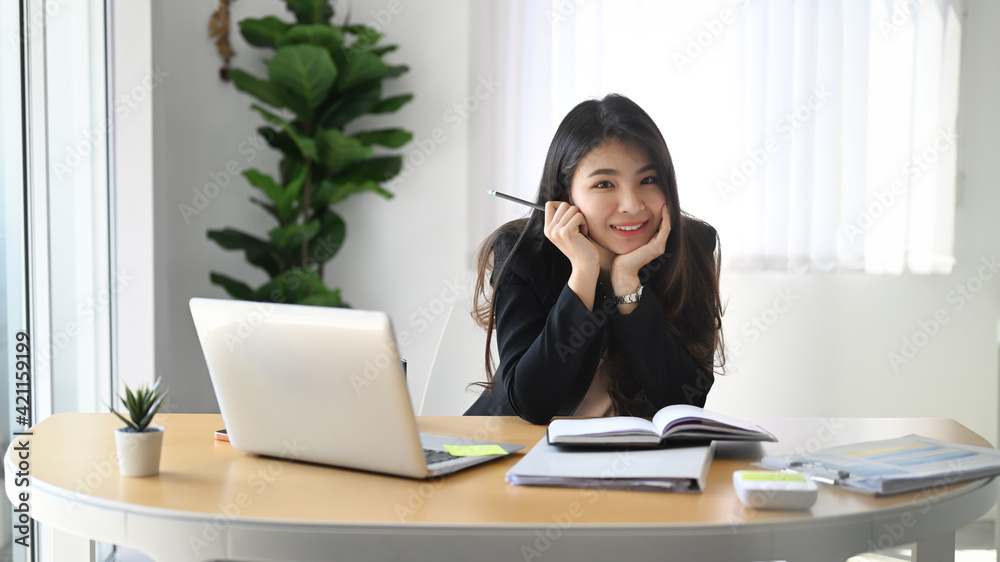 Cheerful young businesswoman sitting at her modern workplace and smiling to camera. Cheerful young businesswoman sitting at her modern workplace and smiling to camera.