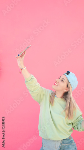 MUJER HERMOSA SONRIENDO TOMANDOSE SELFIE CON CELULAR EN MANO SOBRE FONDO ROSA 
