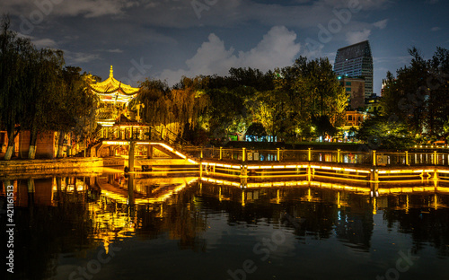 Green lake park scenic view at night with illuminated path and pavilion over a pond Kunming Yunnan China