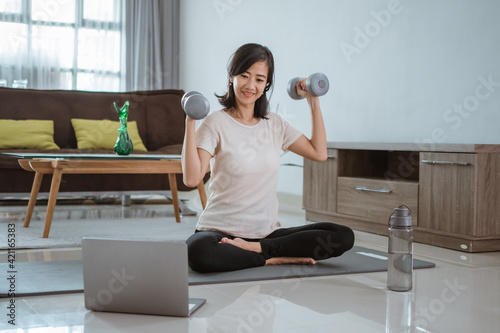 Young girl looking at laptop and doing exercises at home by her self
