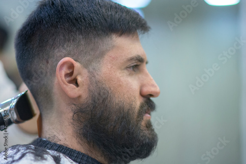 Portrait of a Bearded Caucasian Man with black hair, having a haircut 