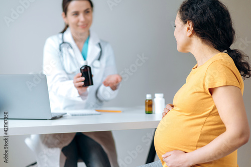 Healthcare of pregnant adult woman. Mixed race pregnant woman in sits at doctor's appointment, receiving consultation and treatment, defocused female doctor sitting at a table giving consultation