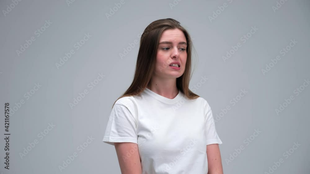 Portrait of funny confused thoughtful shy shamed young girl 20s woman wearing white t-shirt bite lips saying oups I am sorry isolated on white grey background in studio. Natural beauty and emotions. Portrait of funny confused thoughtful shy shamed young girl 20s woman wearing white t-shirt bite lips saying oups I am sorry isolated on white grey background in studio. Natural beauty and emotions.