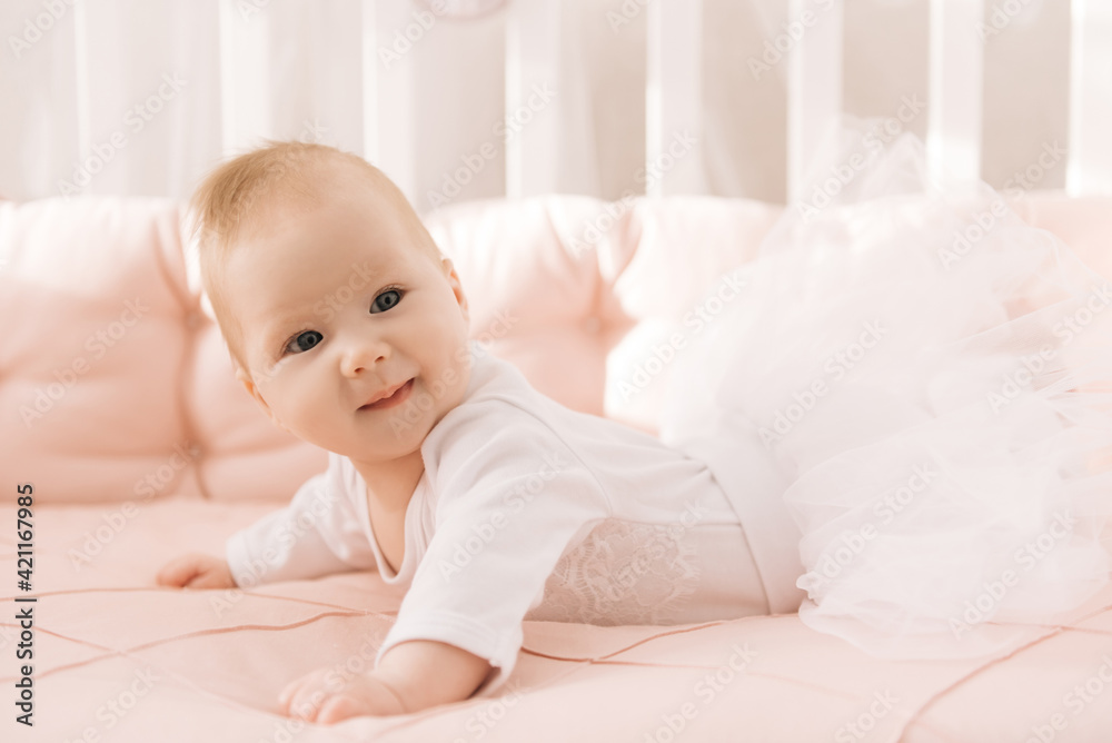 Portrait of a cute 6-month-old baby, a newborn girl lying in a baby crib