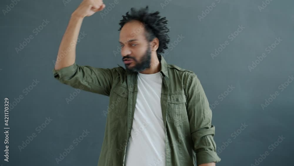 Slow motion portrait of Middle Eastern macho demonstrating biceps and kissing muscles standing on gray background. People and body-building concept.