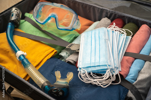 View of a suitcase prepared for a seaside holiday during a pandemic. Neatly folded clothing, packaging of medical masks and snorkeling gear. The concept of a safe holiday at sea.