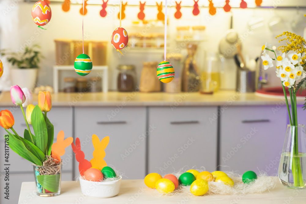 Happy Easter. Festive decorated interior in kitchen in the house, for holiday spring. Garland, painted eggs, greens, flowers on the table