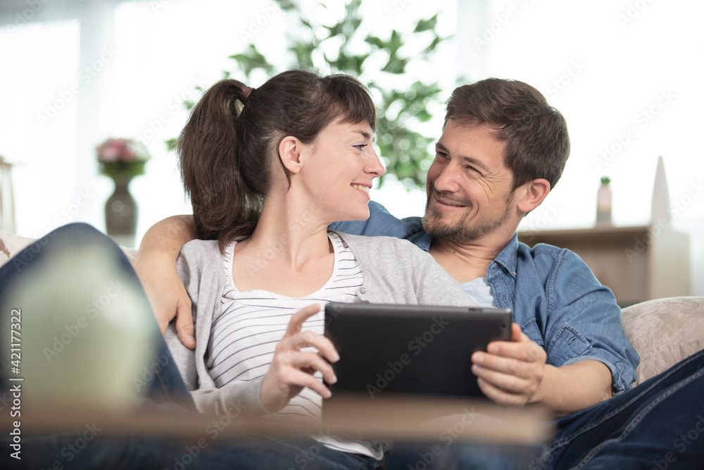 couple snuggled on the sofa looking at a tablet couple snuggled on the sofa looking at a tablet