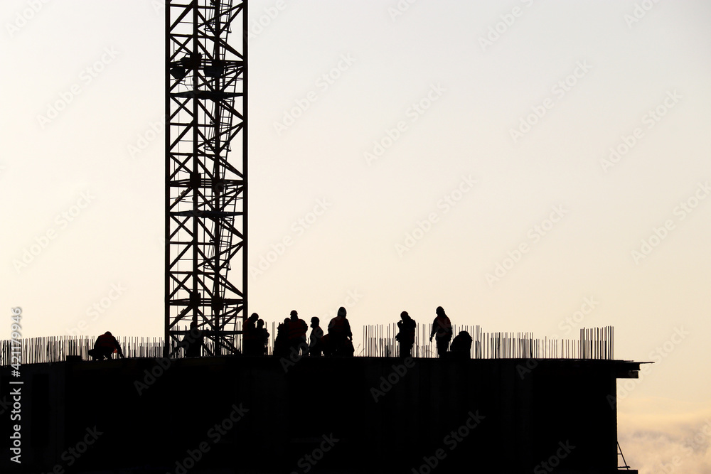 Obraz premium Silhouettes of workers on construction site against the sky. Housing construction, builders working on scaffolding