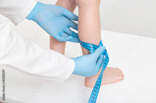 The doctor measures the thickness of the legs of a girl 4 years old with a measuring tape on a white background. The concept of proper nutrition and metabolism of the child.  photo