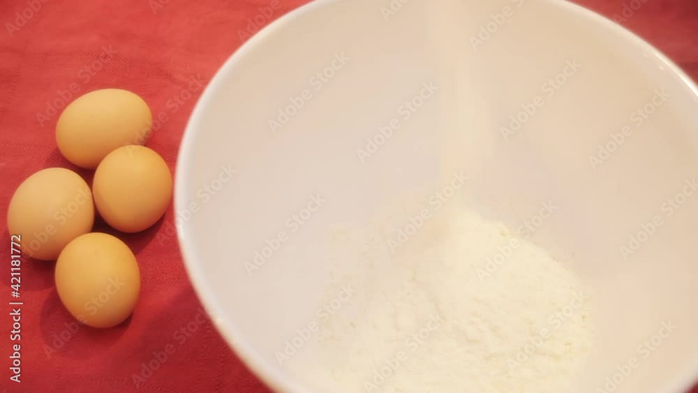 Baking a cake: pouring flour in a cup, with four eggs ready at one side.
Baking a cake: pouring flour in a cup, with four eggs ready at one side.