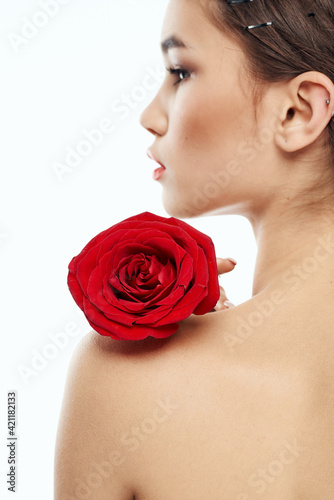 Nude brunette woman with red flower on her shoulder and bright makeup