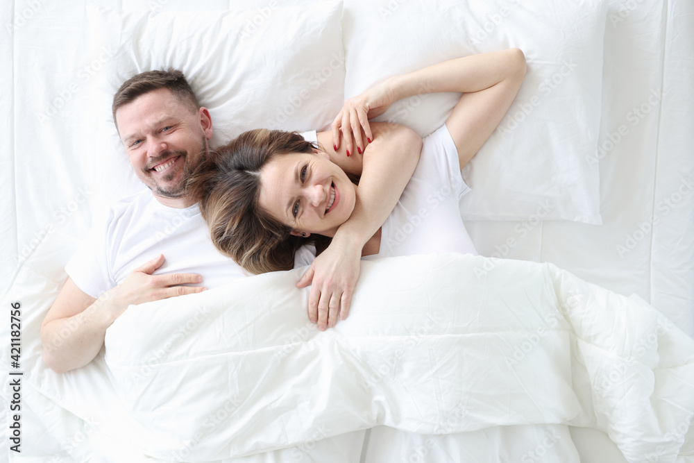 Smiling and happy man and woman lie in an embrace on bed