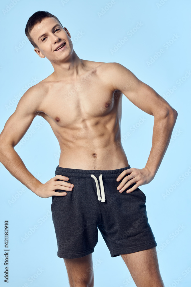 sportsman in shorts on blue background holds hands on belt cropped view