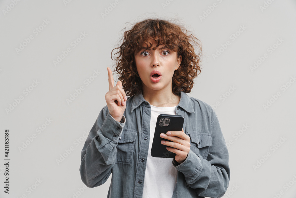 Young shocked woman pointing finger upward while using mobile phone Young shocked woman pointing finger upward while using mobile phone