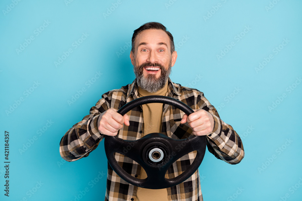 Photo portrait of aged man driving car keeping steering wheel smiling isolated on vivid blue color background Photo portrait of aged man driving car keeping steering wheel smiling isolated on vivid blue color background