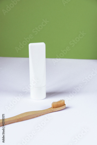 White tube of toothpaste and toothbrush on white table against green wall background. Personal hygiene and self-care concept