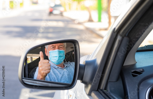Elderly man wearing a protective mask while driving the car looking at the camera in the mirror © luciano