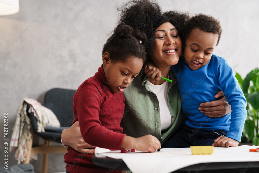 Happy afro american mother hugging while drawing with her children Happy afro american mother hugging while drawing with her children