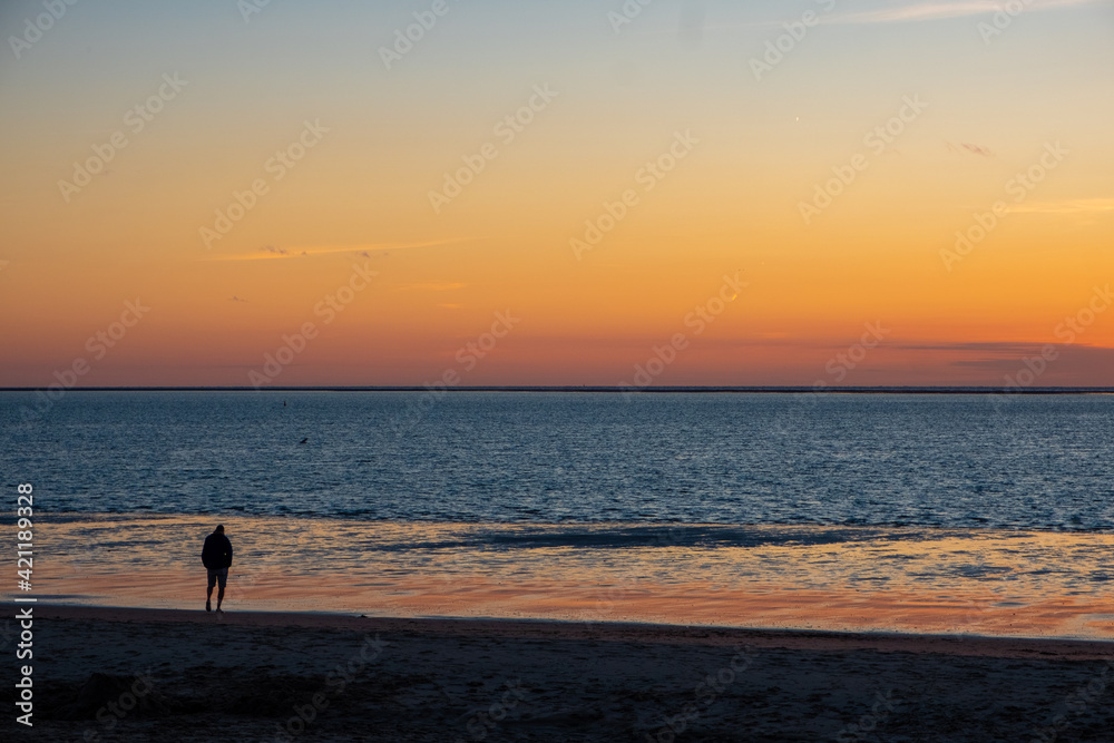 View of silhouettes of people walking in the setting sun shining on the Sea and reflected on the beach, clouds with sun-shining edges. Landscape. High quality photo showing concept of freedom and