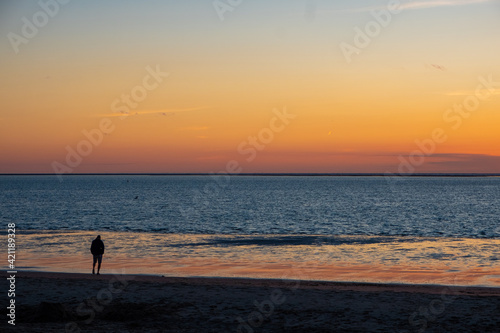 View of silhouettes of people walking in the setting sun shining on the Sea and reflected on the beach, clouds with sun-shining edges. Landscape. High quality photo showing concept of freedom and